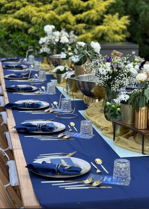 Lange festliche Tafel im Freien mit blauer Tischdeko und weißen Blumen